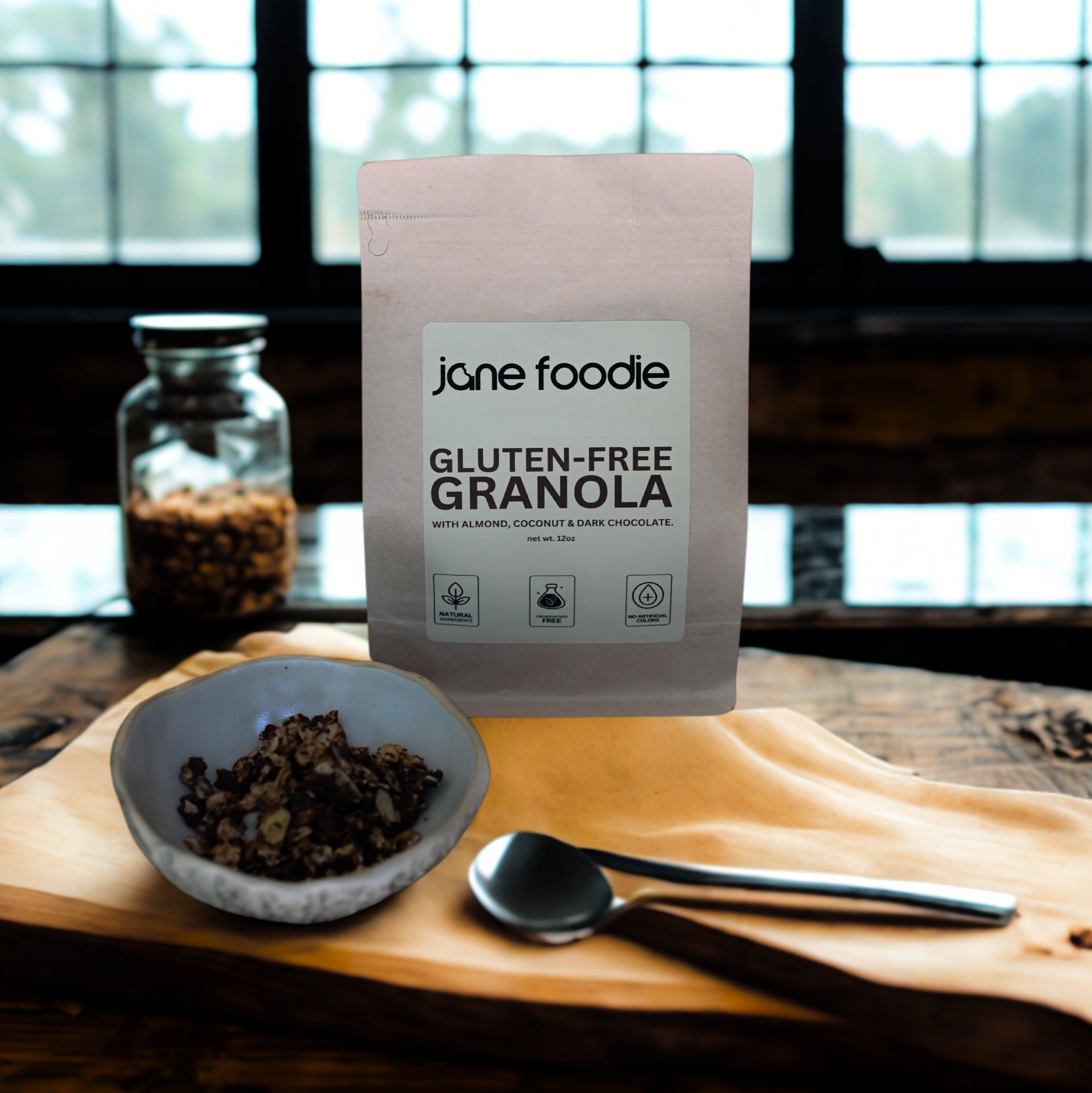 Jane Foodie Pantry Award-winning gluten-free granola with almonds, coconut, and dark chocolate, shown in pouch beside bowl and spoon.