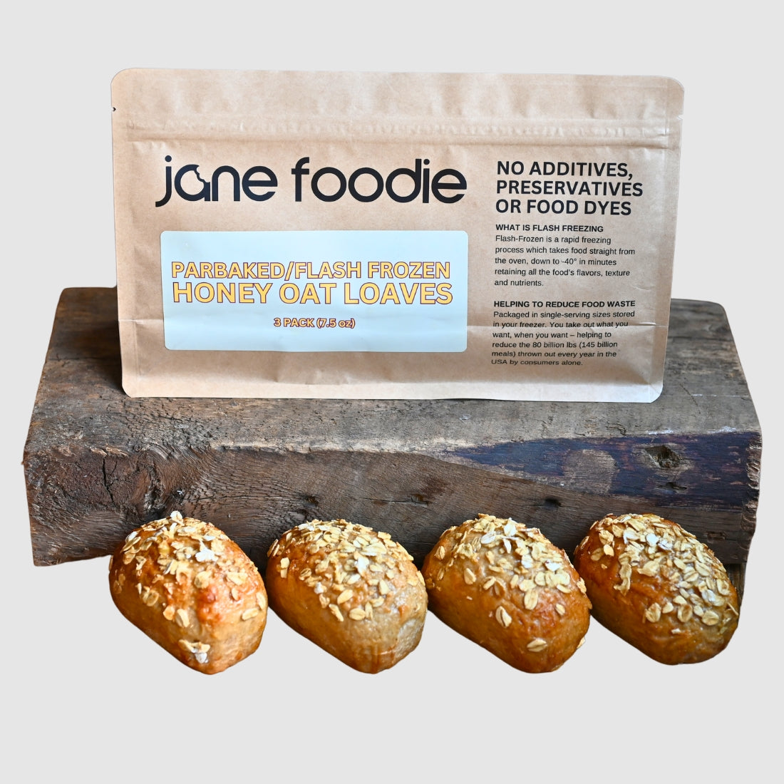 Jane Foodie honey oat mini loaves in a parbaked, flash-frozen 3-pack bag, displayed on a rustic wooden block with neutral background.