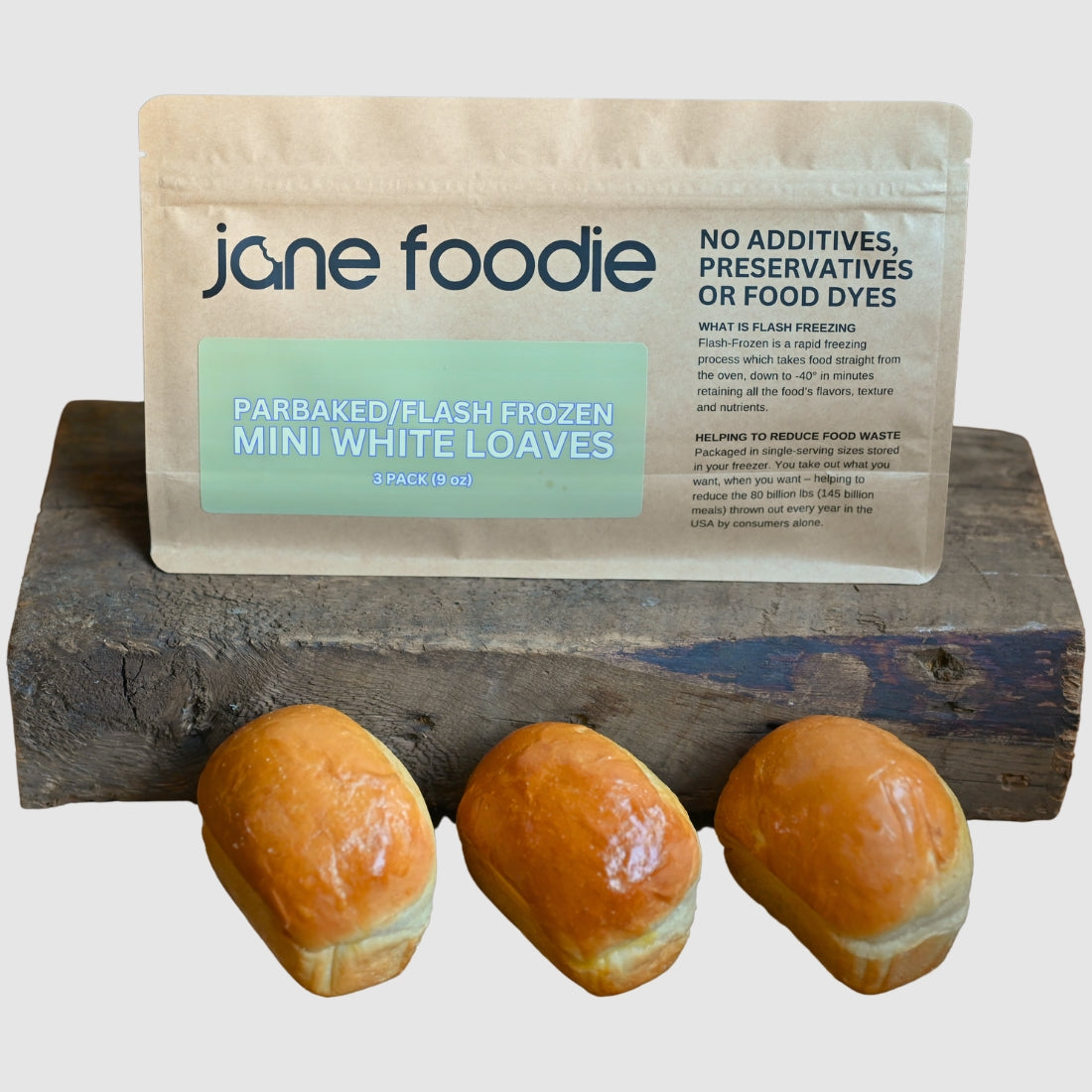 ane Foodie mini white loaves in parbaked, flash-frozen 3-pack bag, displayed on a rustic wooden block with neutral background.
