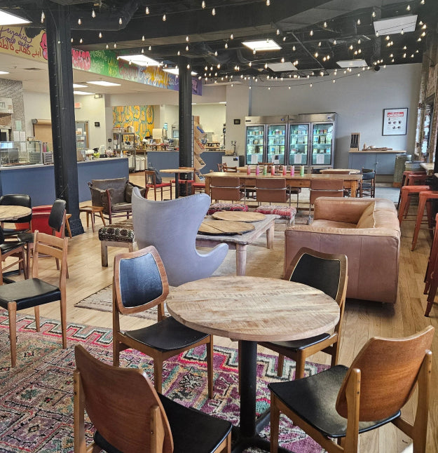Dining area with tables, chairs, and a colorful rug in a casual setting.