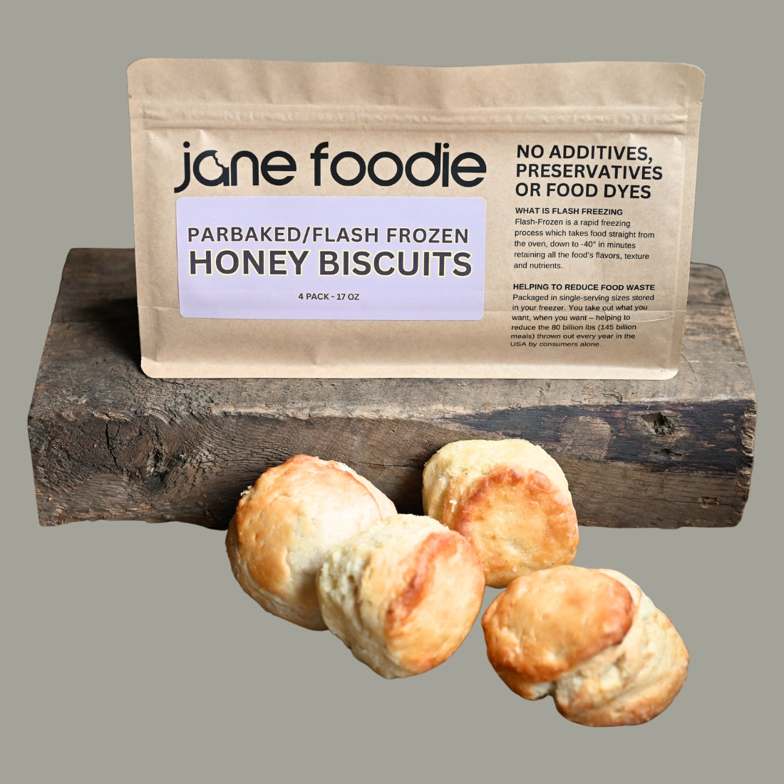 Parbaked flash-frozen honey biscuits in a 4-pack with ‘Jane Foodie’ branded packaging, displayed on a rustic wooden block with a neutral gray background.