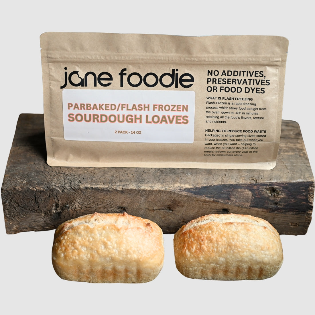 Parbaked/flash frozen sourdough loaves in Jane Foodie packaging, displayed on a rustic wooden block with a neutral gray background