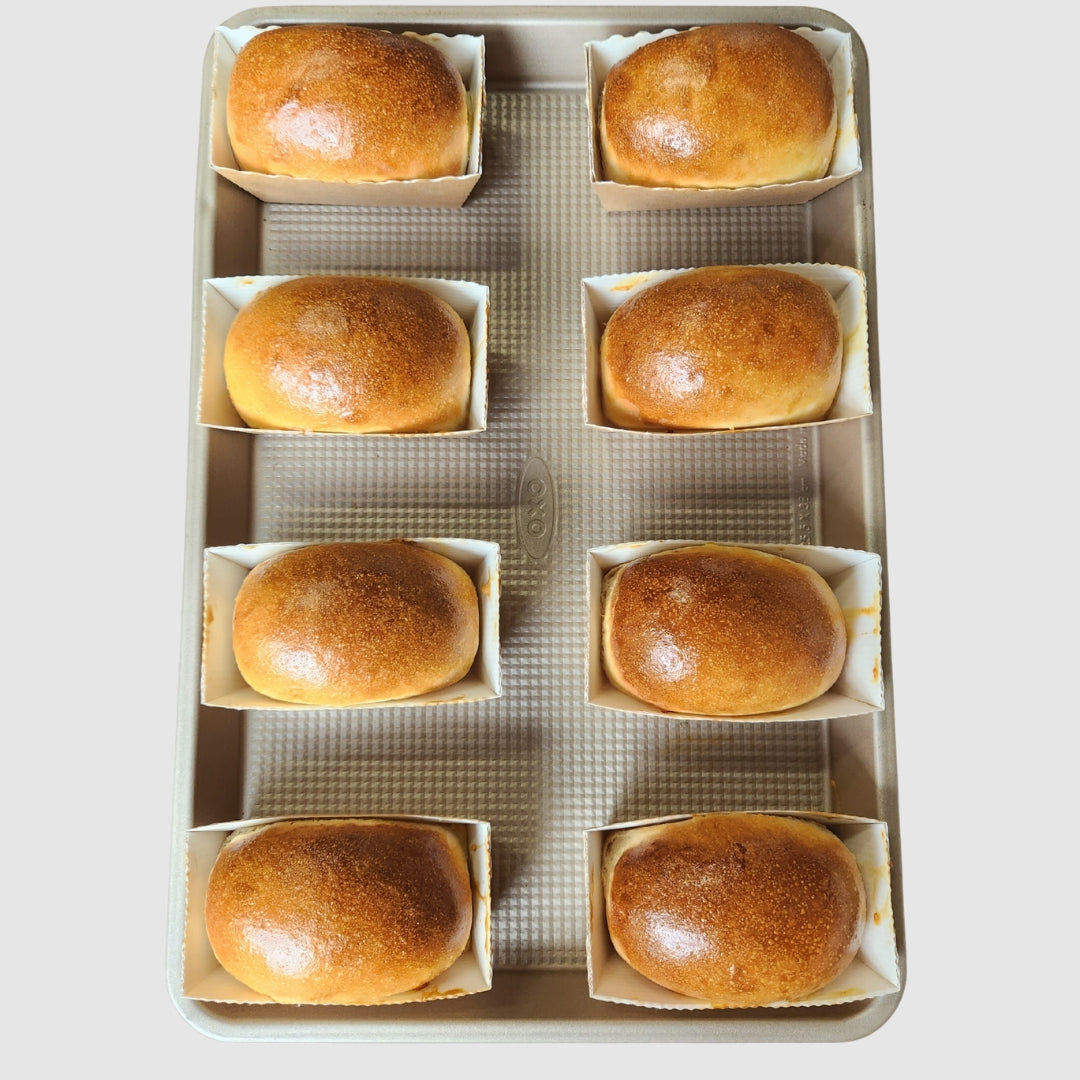 A full tray of parbaked/flash frozen mini white loaves from Jane Foodie, shown in individual baking trays on a sheet pan
